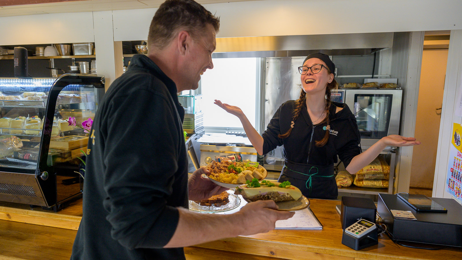 Kunde som handler over disk og snakker med betjeningen på Café Innom